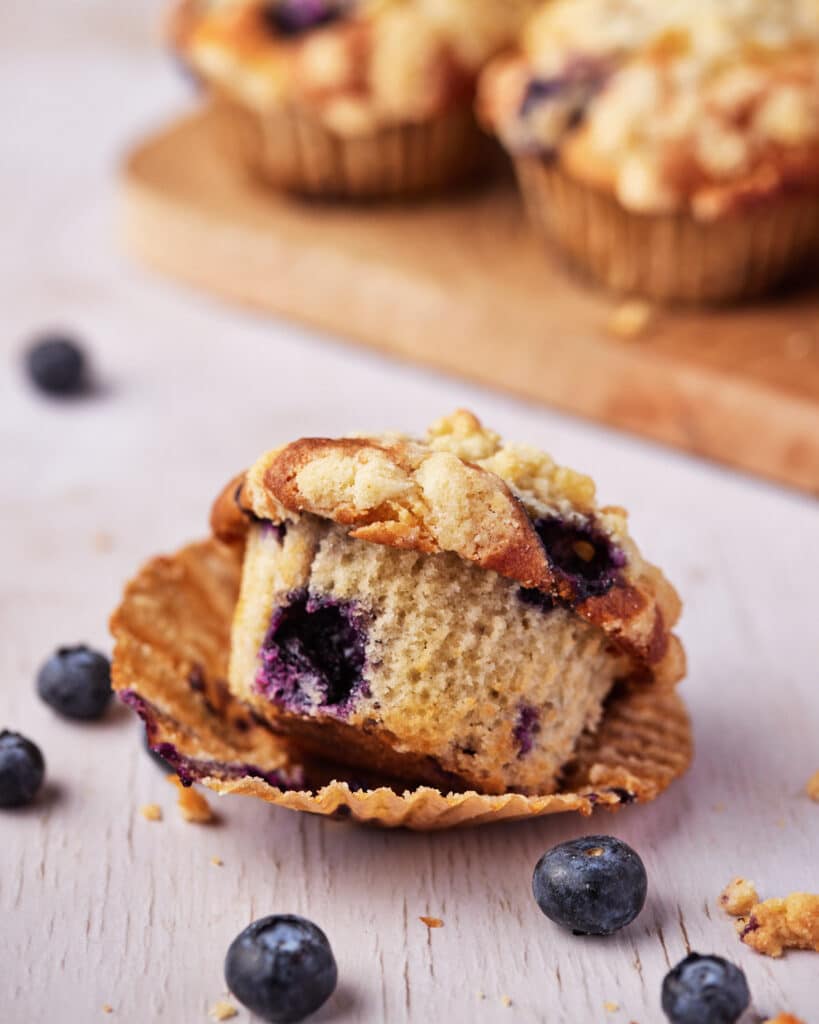 Blueberry Cream Cheese Muffin out of its wrapper, tipped slightly to one side, revealing juicy blueberries in the middle.