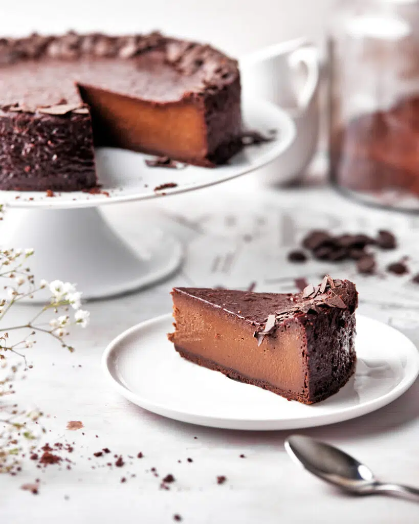 slice of baked chocolate custard tart on a plate with whole chocolate flan in the background