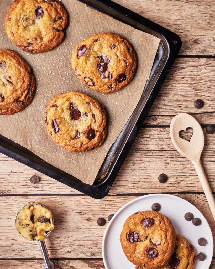 tray of dark chocolate and sea salt cookies on a wooden table with a wooden spoon