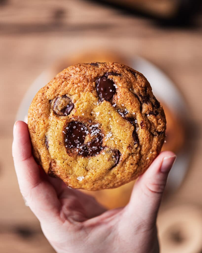 one dark  chocolate chip and sea salt cookie held above a blurred background