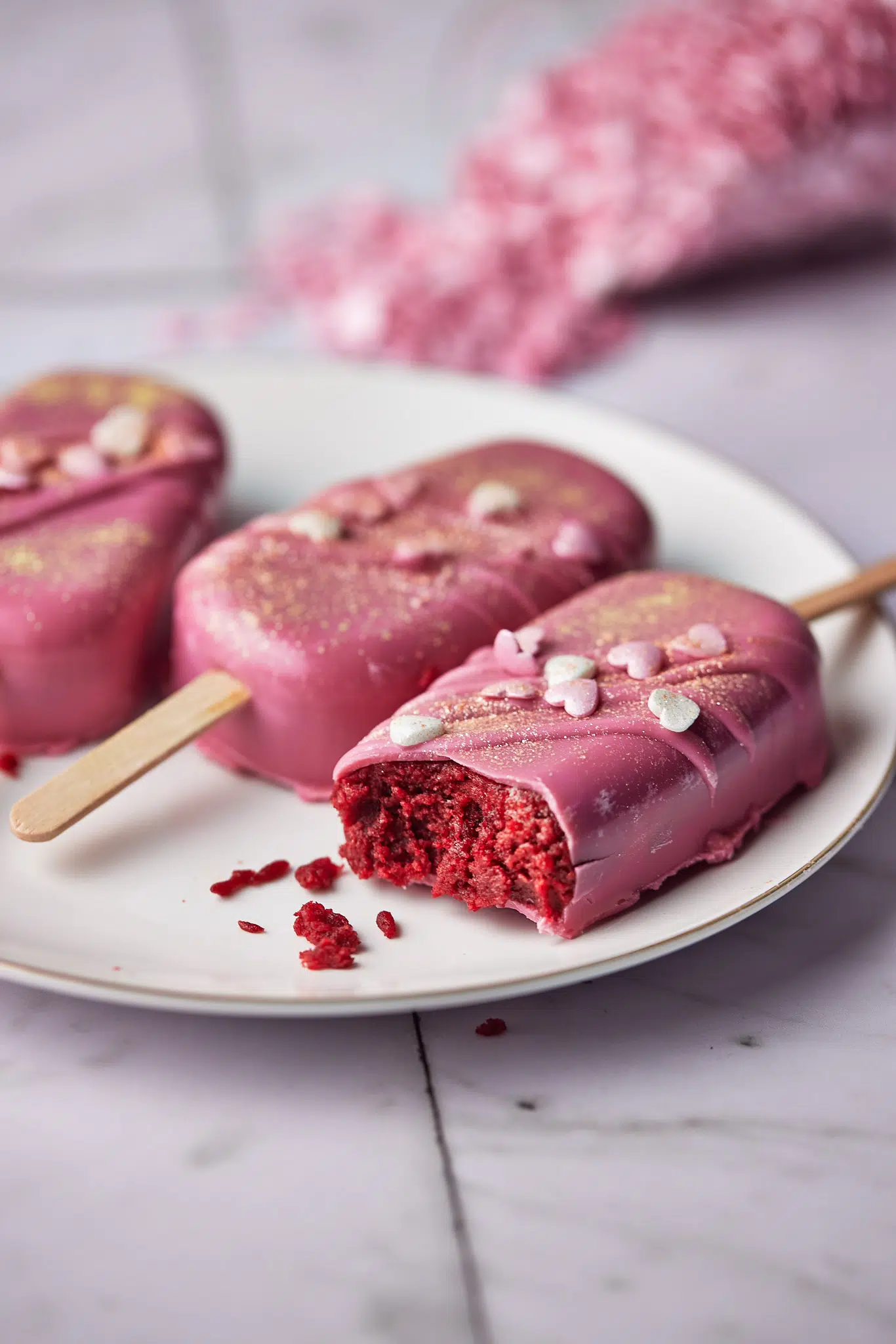 pink valentines cakesicles with a bite out of one, red velvet cake inside