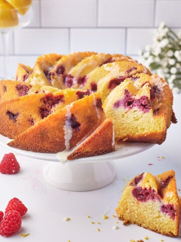lemon raspberry bundt cake on a cake stand with one slice taken out of it.