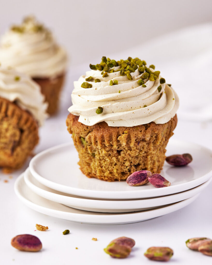 Single pistachio cupcake on three small stacked plates, with pistachios strewn around the background