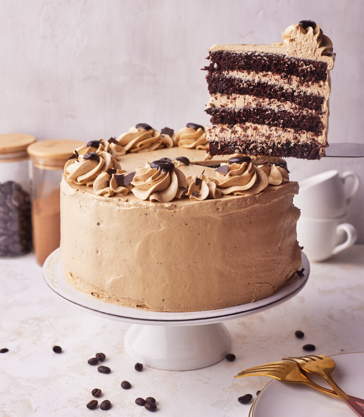 Far away shot of chocolate espresso cake on a cake stand with slice cut out of it on a serving knife.
