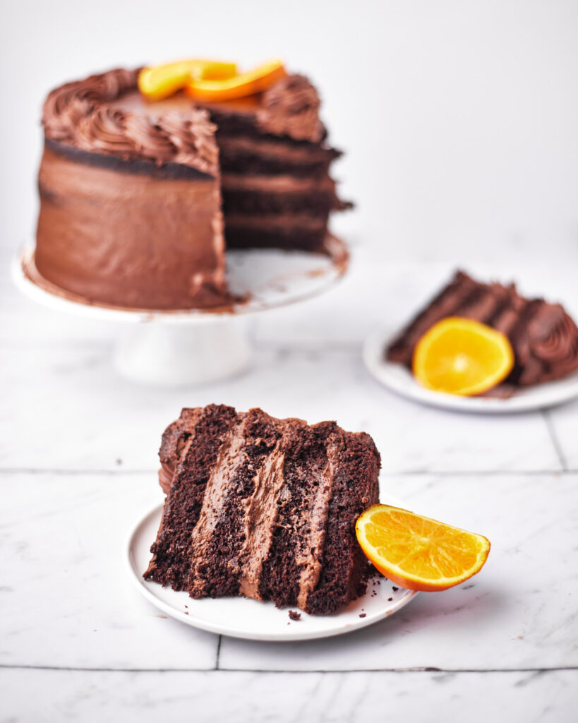 slice of chocolate orange cake with full cake in the background