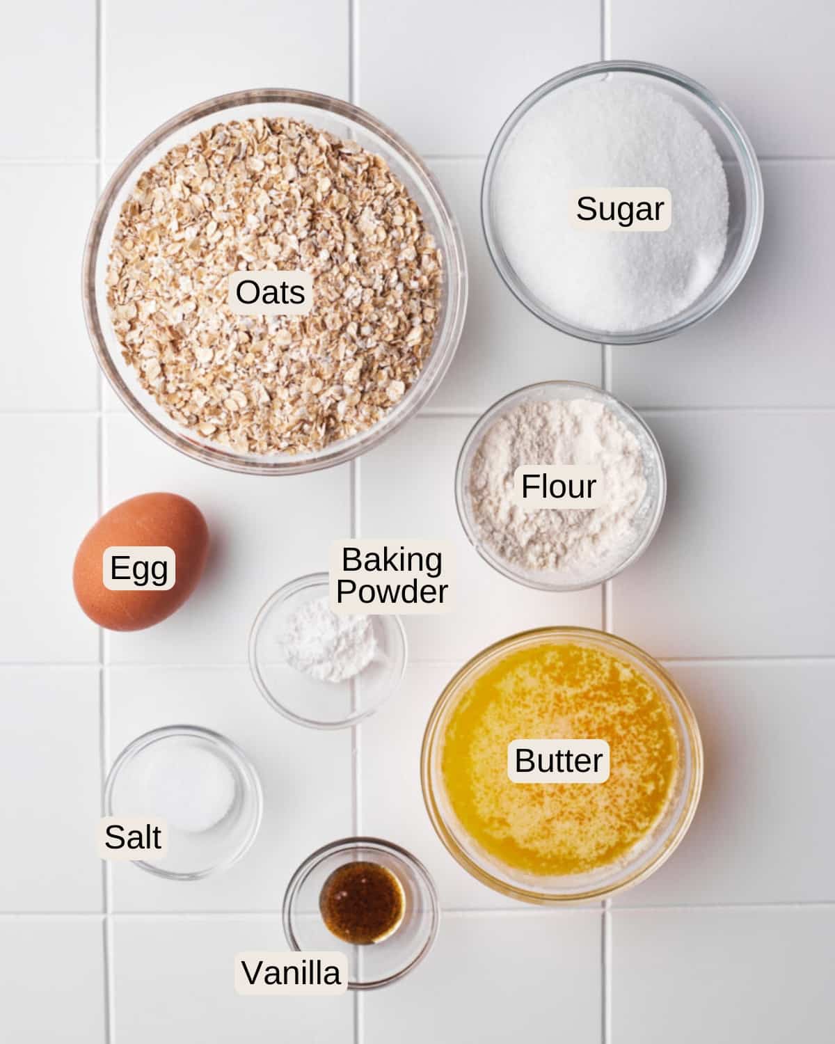 Labelled ingredients for oatmeal lace cookies, including oats, sugar, an egg, flour, baking powder, butter, salt, and vanilla.