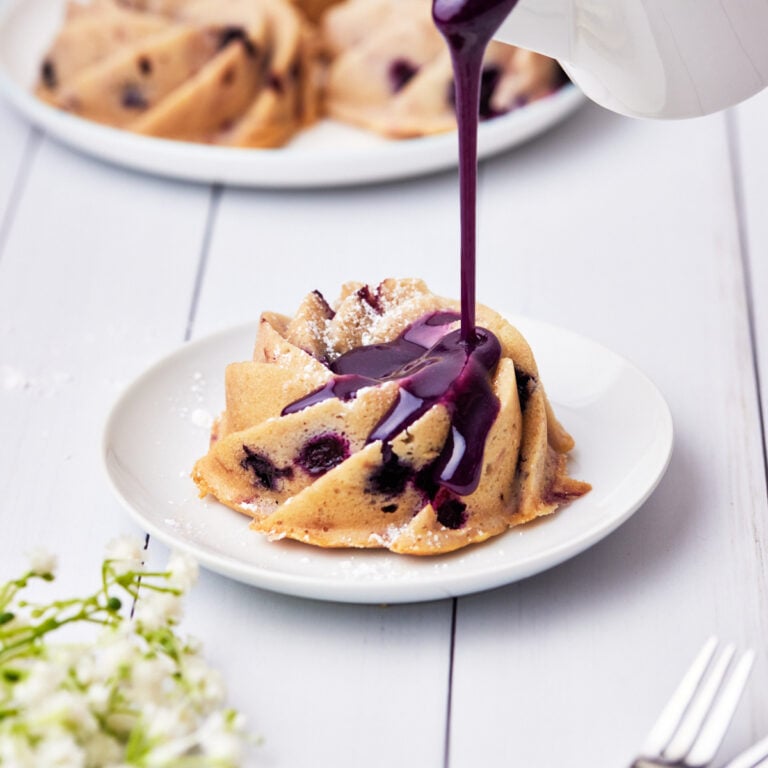 mini blueberry bundt cake with blueberry glaze being poured on top.