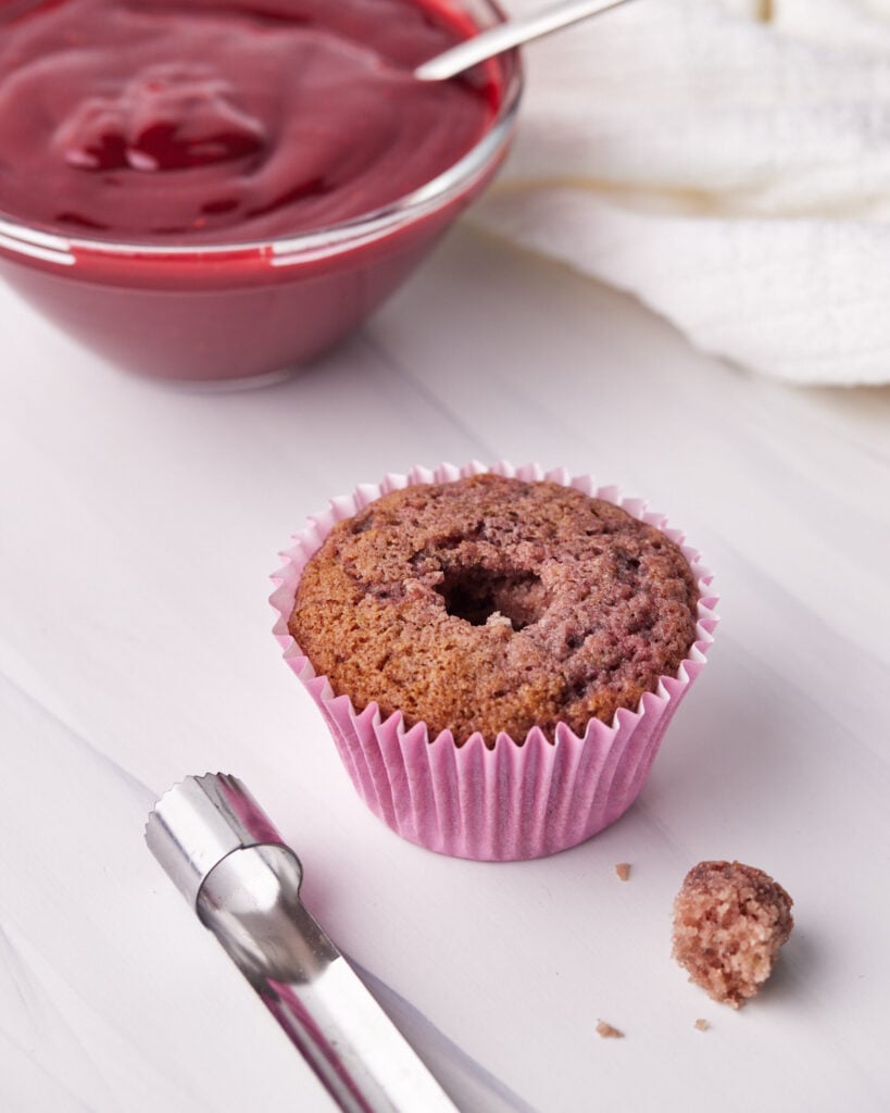 Process shot of how to fill the raspberry cupcakes with raspberry coulis.