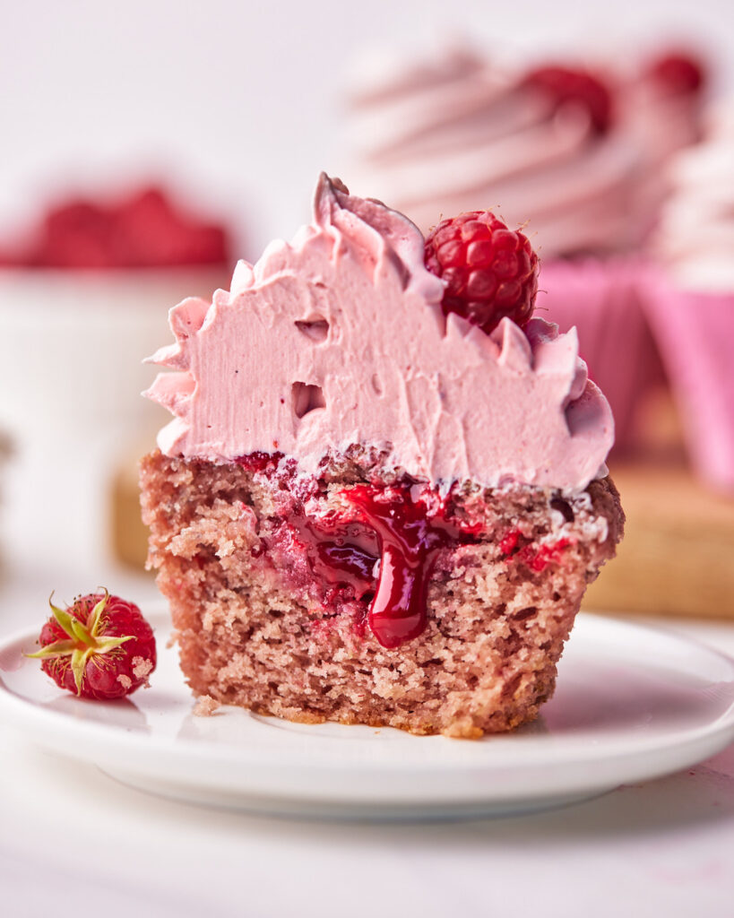 raspberry cupcake sliced in half to reveal raspberry coulis dripping out the middle. 