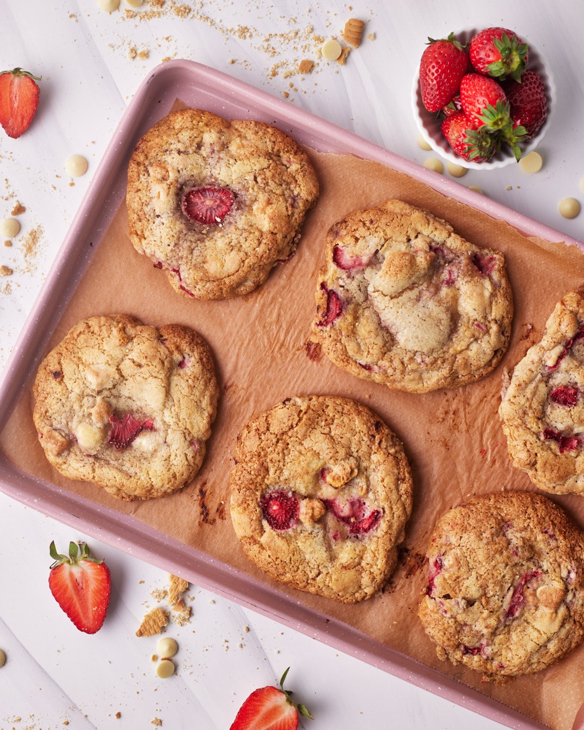 Strawberry cheesecake cookies on a pink baking sheet, from above.