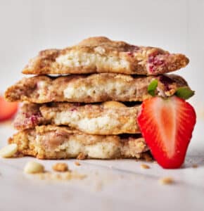 Four strawberry cheesecake cookies in a stack, all cut in half to reveal the cream cheese filling inside.