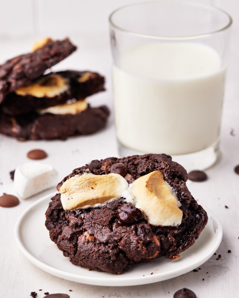 close up of triple chocolate marshmallow cookie with a glass of milk.