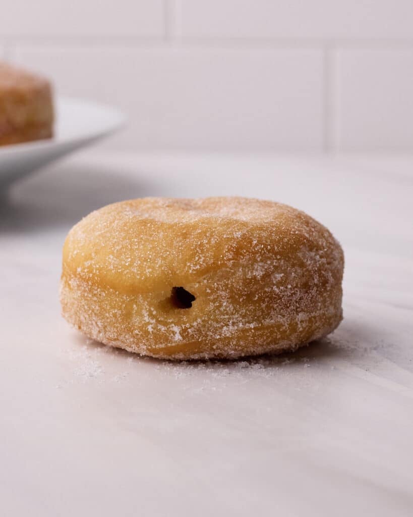 Fried donut with a hole poked in the side to fill it with pastry cream.