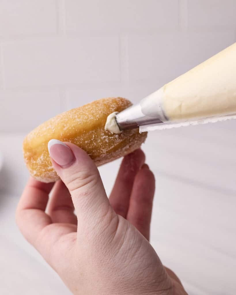 Using a piping bag to pipe pastry cream inside a donut.