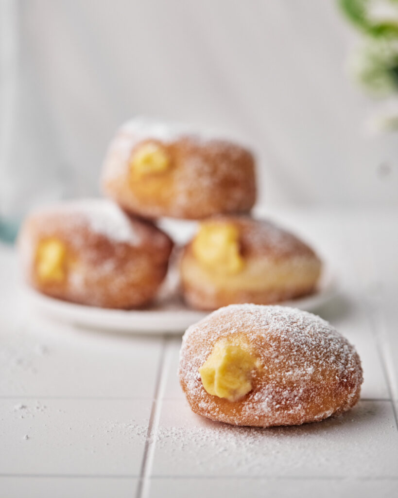 three custard donuts piled on a plate and one in front with custard oozing out. 
