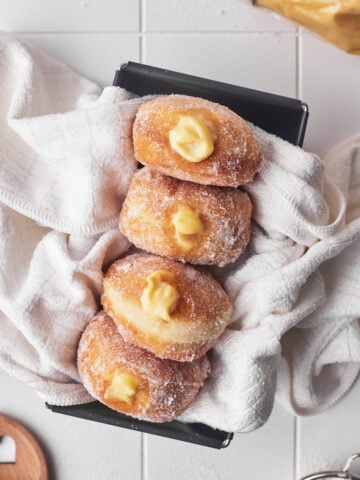 Four custard filled donuts in a baking pan with custard oozing out of them.