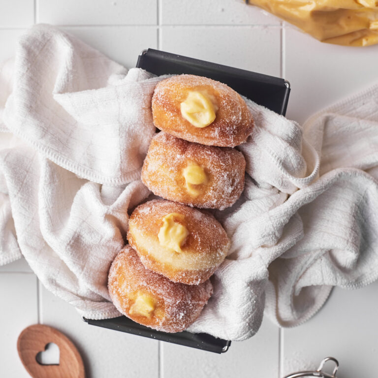 Four custard filled donuts in a baking pan with custard oozing out of them.
