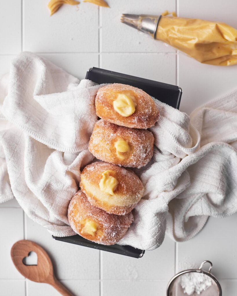 Four custard donuts in a pan, from above with custard filling bursting out. 
