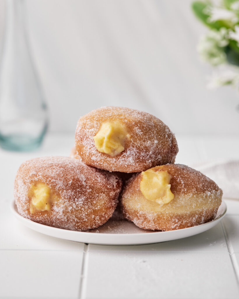 three custard donuts on a plate with filling spilling out. 