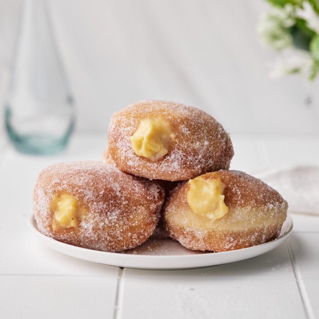 Three custard donuts sitting on a plate with custard filling oozing out of them.