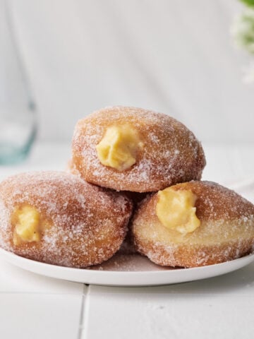 Three custard donuts sitting on a plate with custard filling oozing out of them.