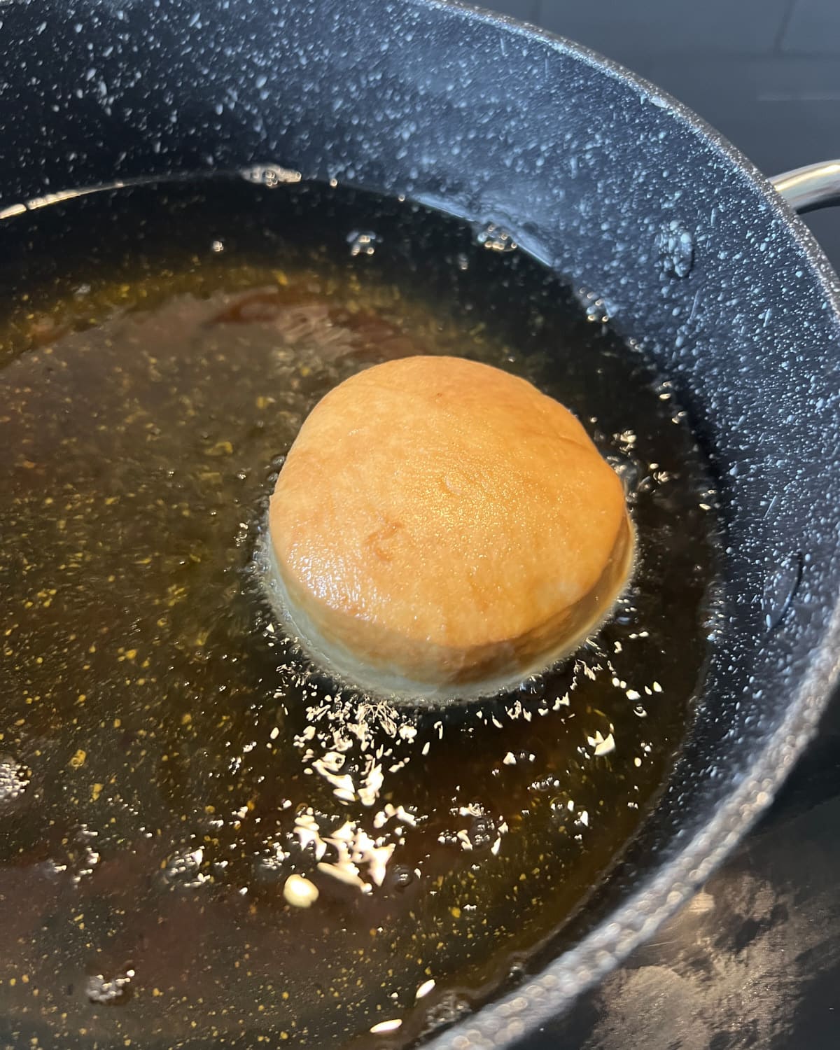 One donut frying in oil until golden brown.