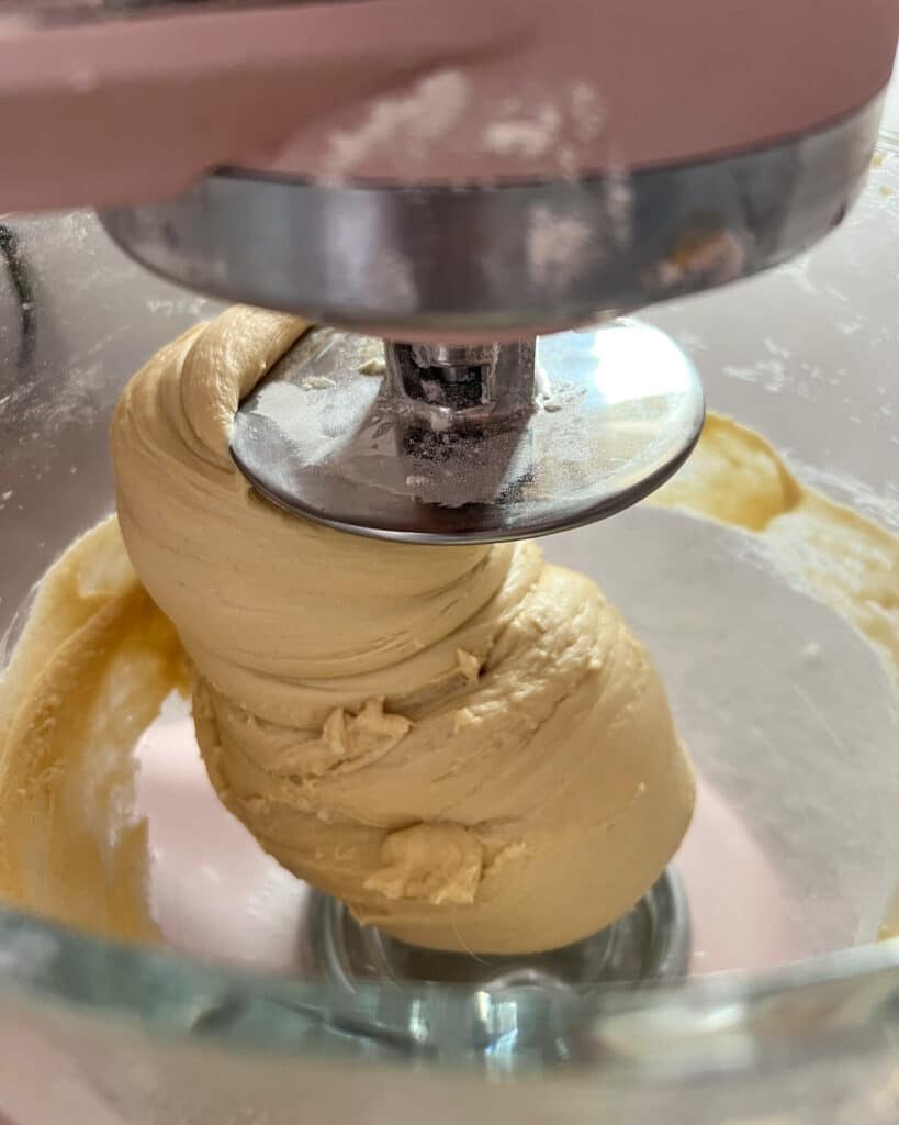 Mixing bowl showing donut dough on a dough hook, no longer sticking to the side of the bowl.