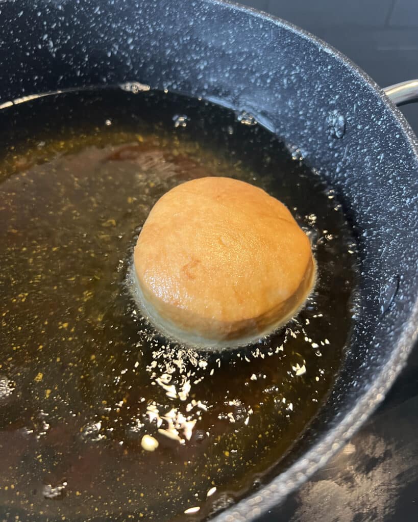 Yeast donut frying in hot oil, one side is light golden brown. 