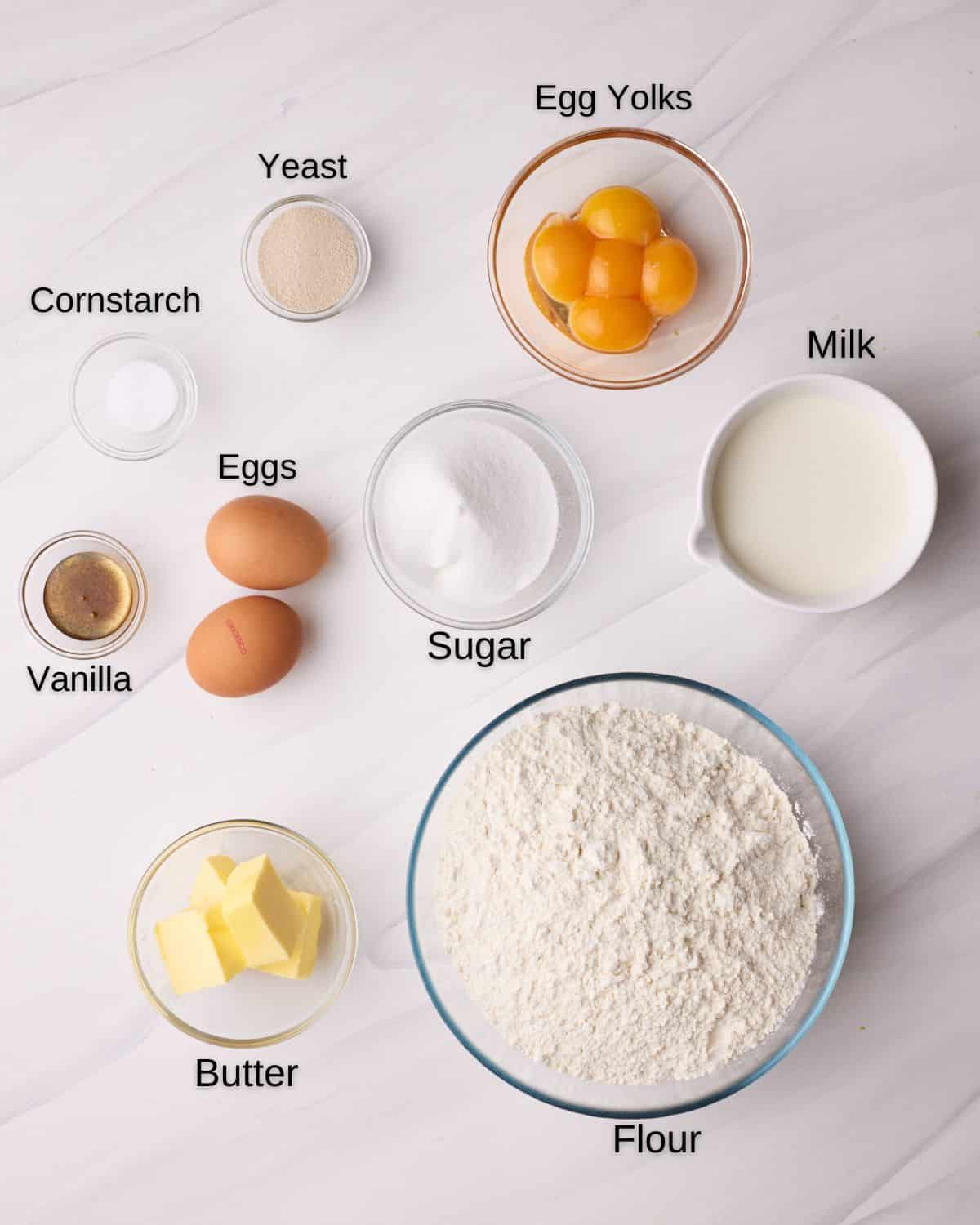 Ingredients to make custard donuts - flour, butter, milk, sugar, eggs, vanilla, yeast, cornstarch, egg yolks and milk. 