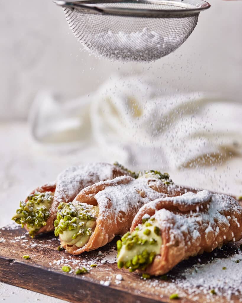 pistachio cannoli being dusted with icing sugar.