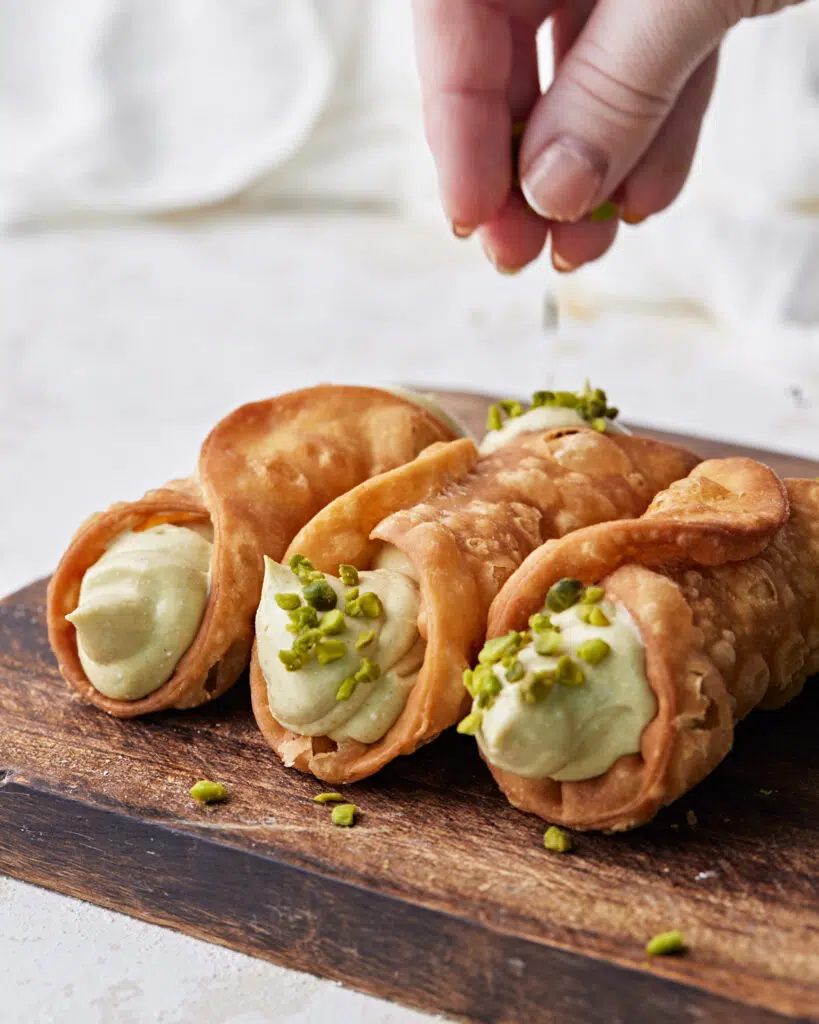 chopped pistachios being sprinkled on the ends of pistachio cannoli.