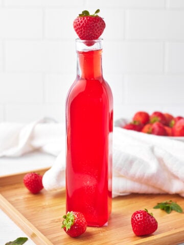 strawberry simple syrup in a glass bottle with a fresh strawberry on top.