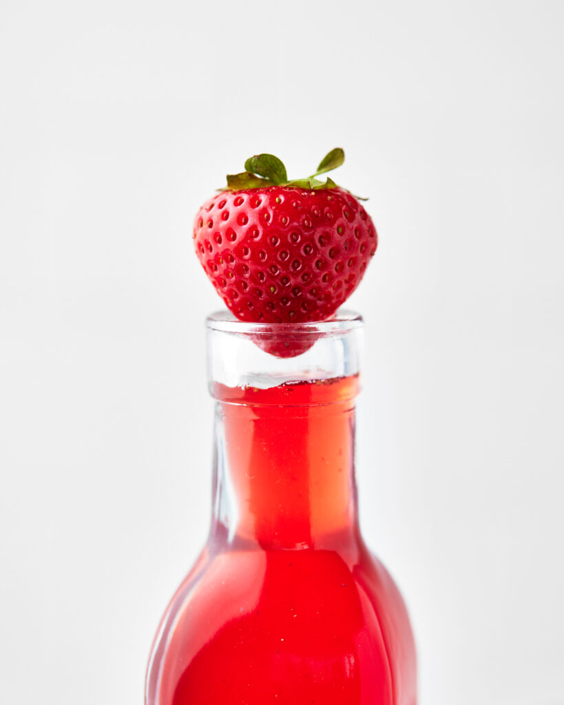 top of a bottle of homemade strawberry simple syrup with a fresh strawberry in the bottle.