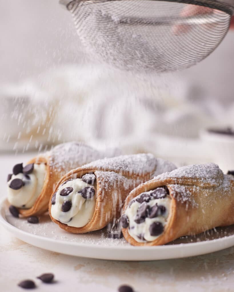 air fryer cannoli being dusted with powdered sugar.