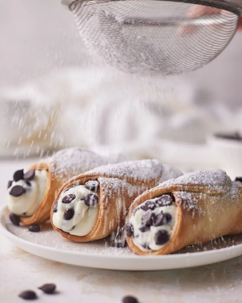 air fryer cannoli being dusted with powdered sugar.