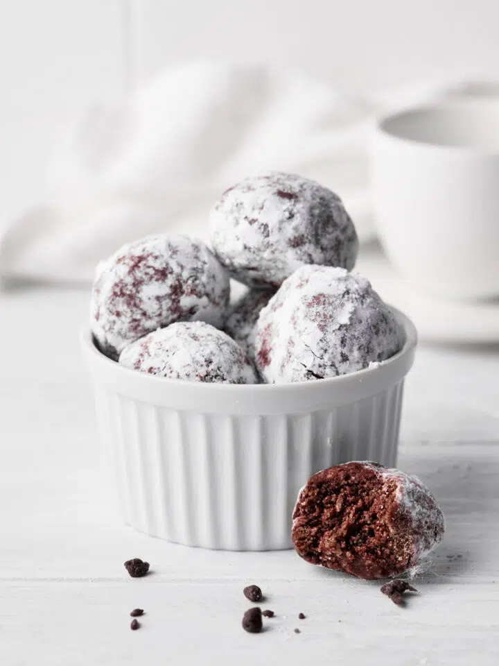 Chocolate balls in a small bowl with one with a bite taken out.