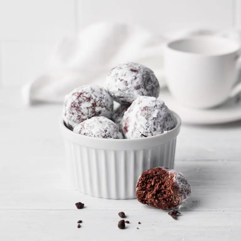 Chocolate balls in a small bowl with one with a bite taken out.