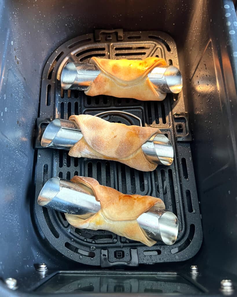cooked cannoli shells in air fryer basket.