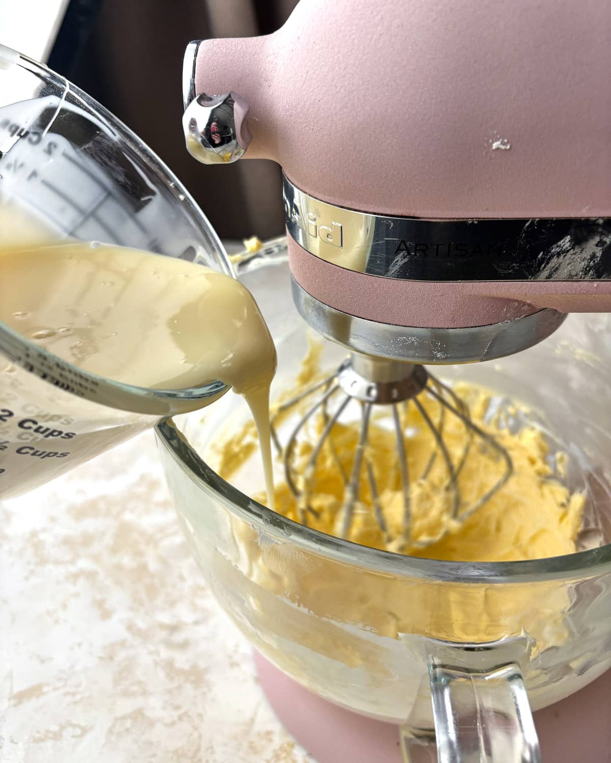 Pouring sweetened condensed milk into whipped butter very slowly to make Russian buttercream.