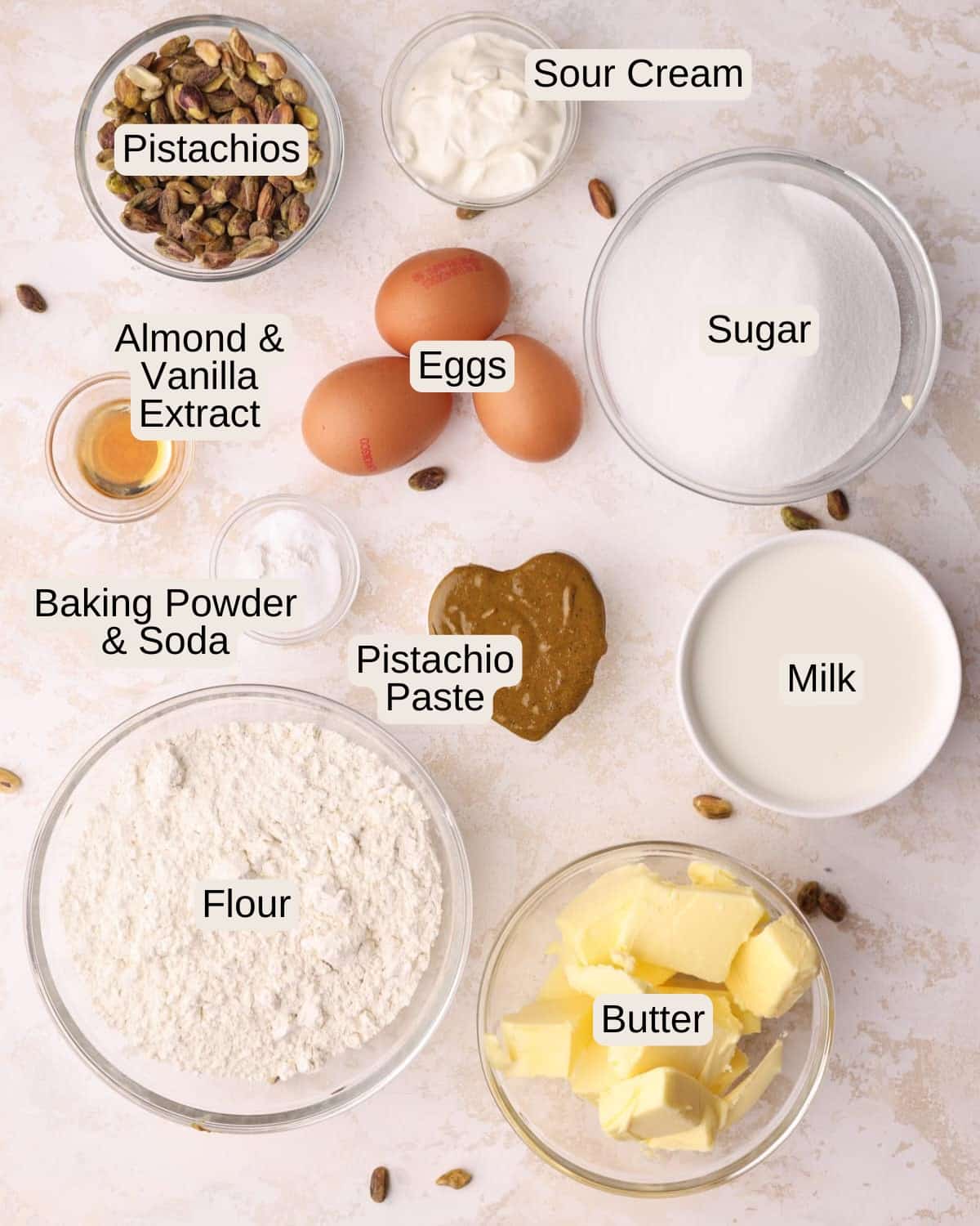 Ingredients to make pistachio cake, including flour, sugar, butter, pistachio paste, eggs, salt, sour cream, vanilla extract and almond extract.