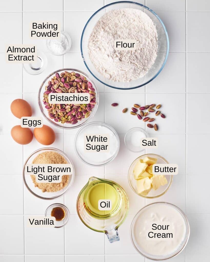 Labelled ingredients for pistachio muffins, including Pistachios, Light Brown Sugar, White Sugar, Salt, Vanilla, Eggs, Flour, Butter, Oil, Sour Cream, Almond Extract, and Baking Powder.
