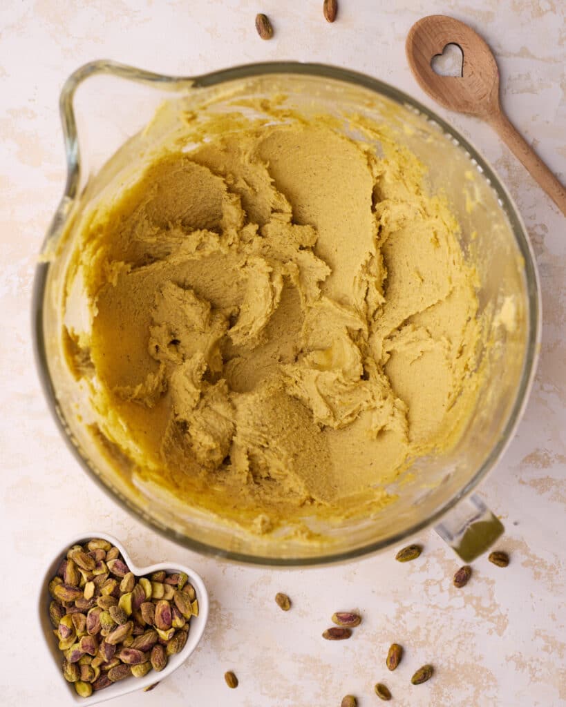 Butter, sugar, and pistachio paste creamed together in a glass mixing bowl until light and fluffy to make pistachio cake.