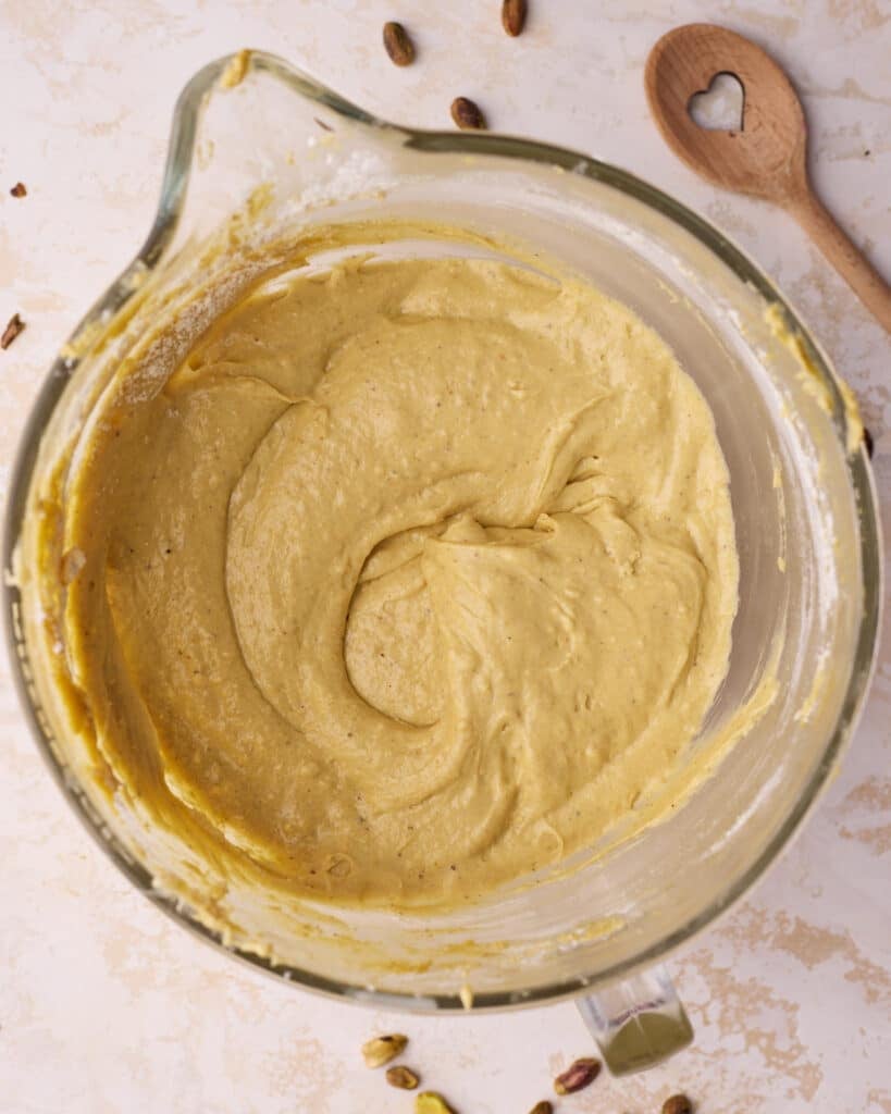 Pistachio cake batter in a glass mixing bowl, showing the soft texture after adding the eggs.