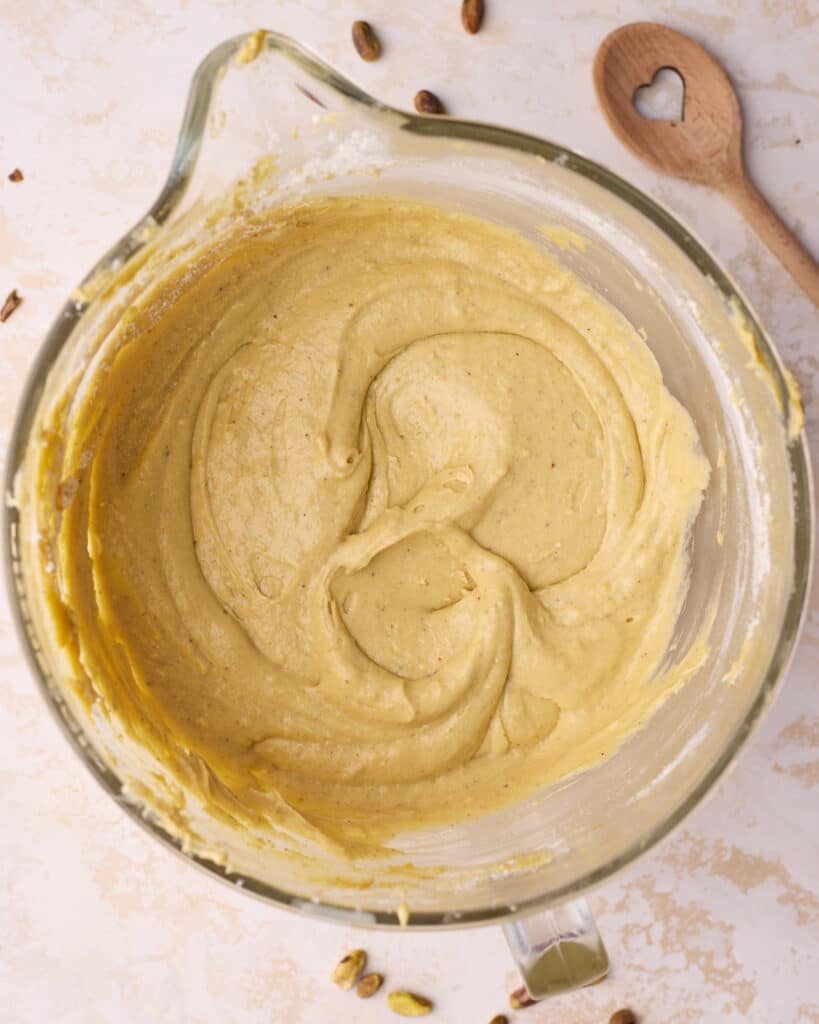 Pistachio cake batter in a mixing bowl, thick and glossy with a pale green colour.