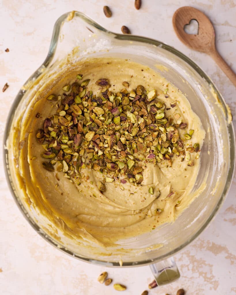 Chopped pistachio nuts being added to pistachio cake batter.