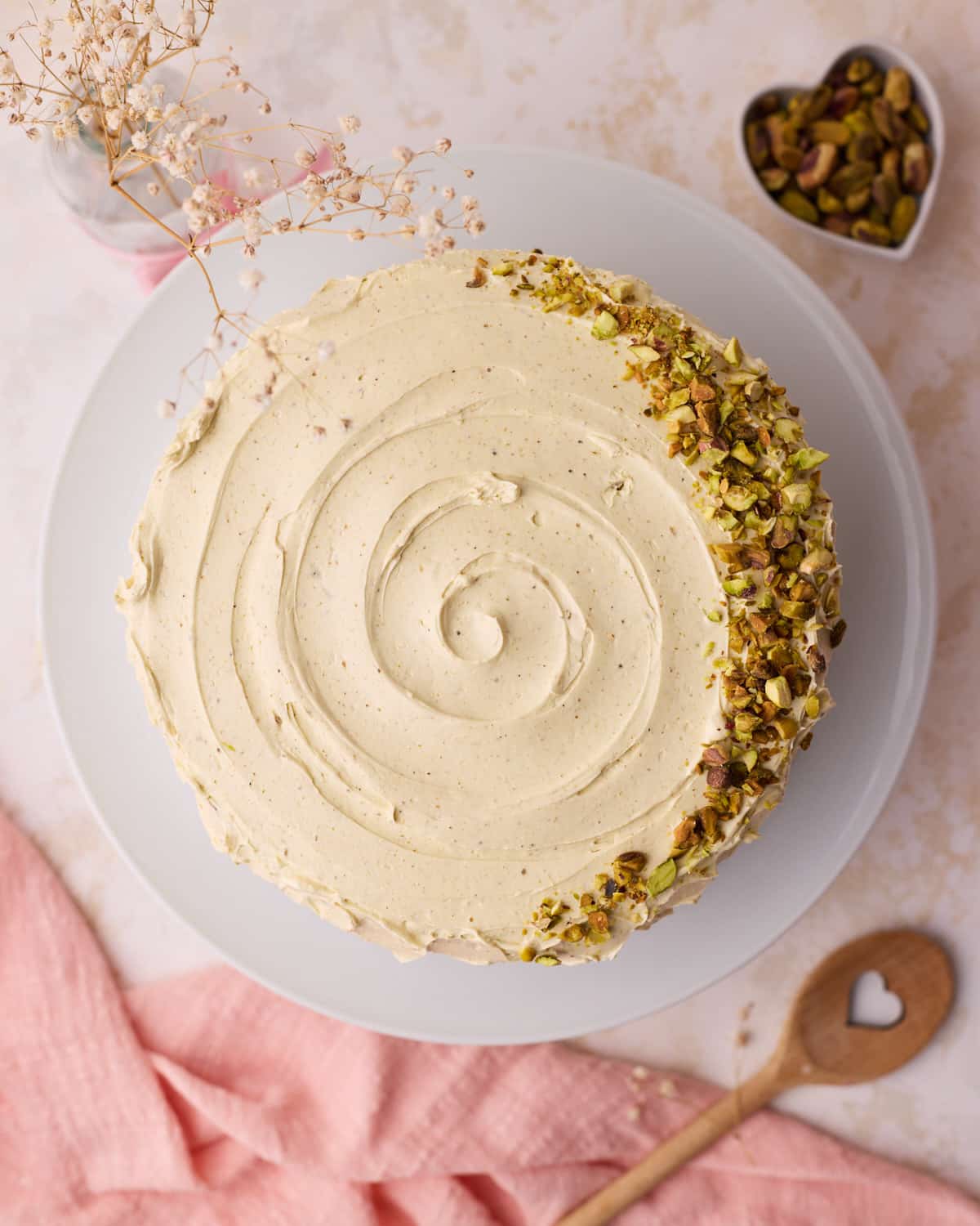 Overhead view of a pistachio cake with pistachio buttercream swirled on top, and a crescent of chopped pistachios to decorate.
