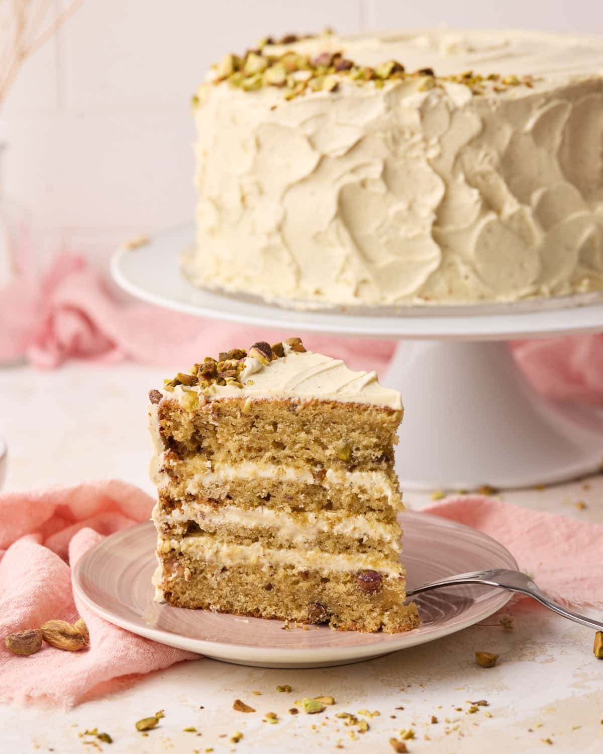 Slice of pistachio cake on a plate with four thin layers of cake and Italian meringue buttercream.