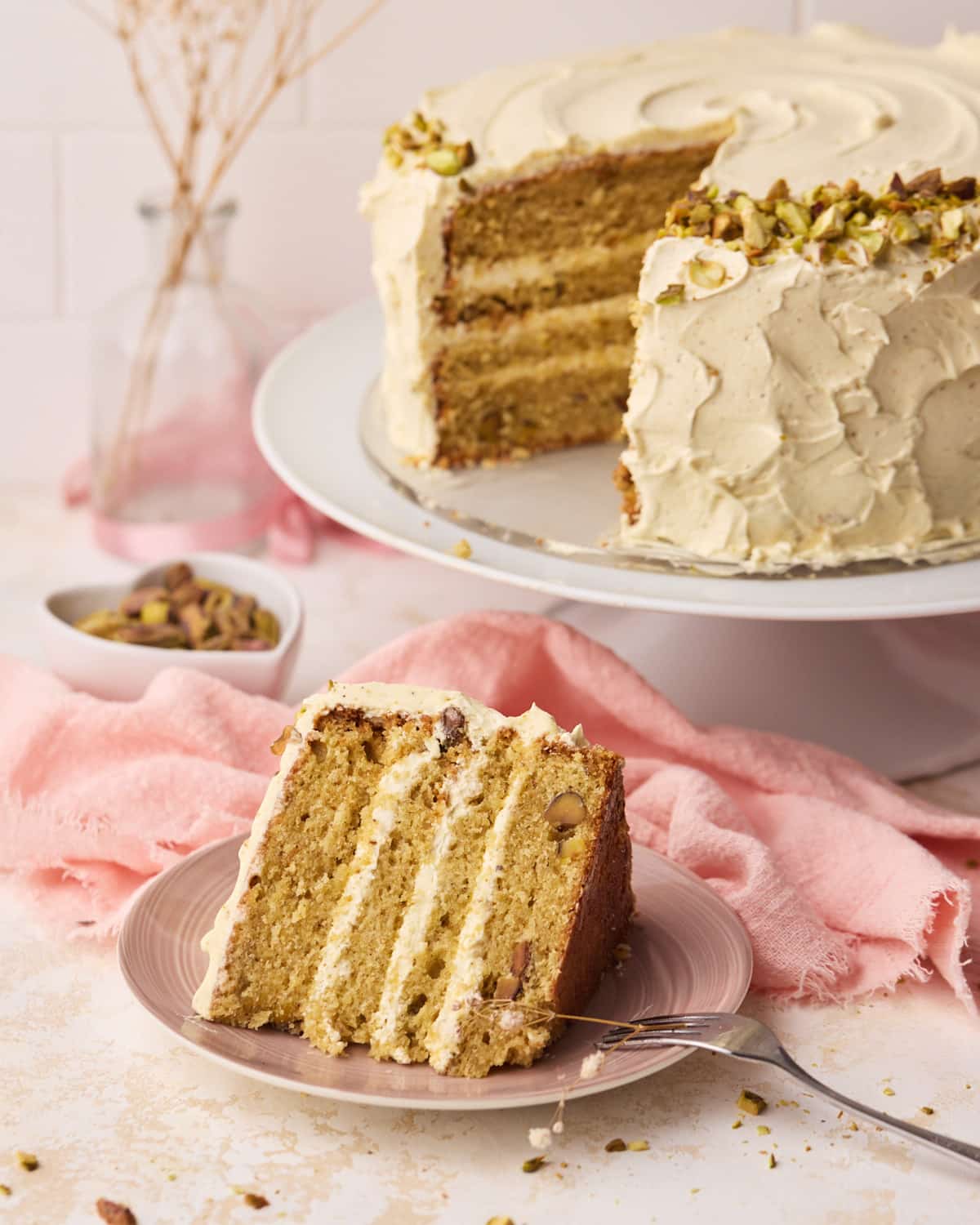 Slice of pistachio cake on a plate with four thin layers of cake and Italian meringue buttercream.