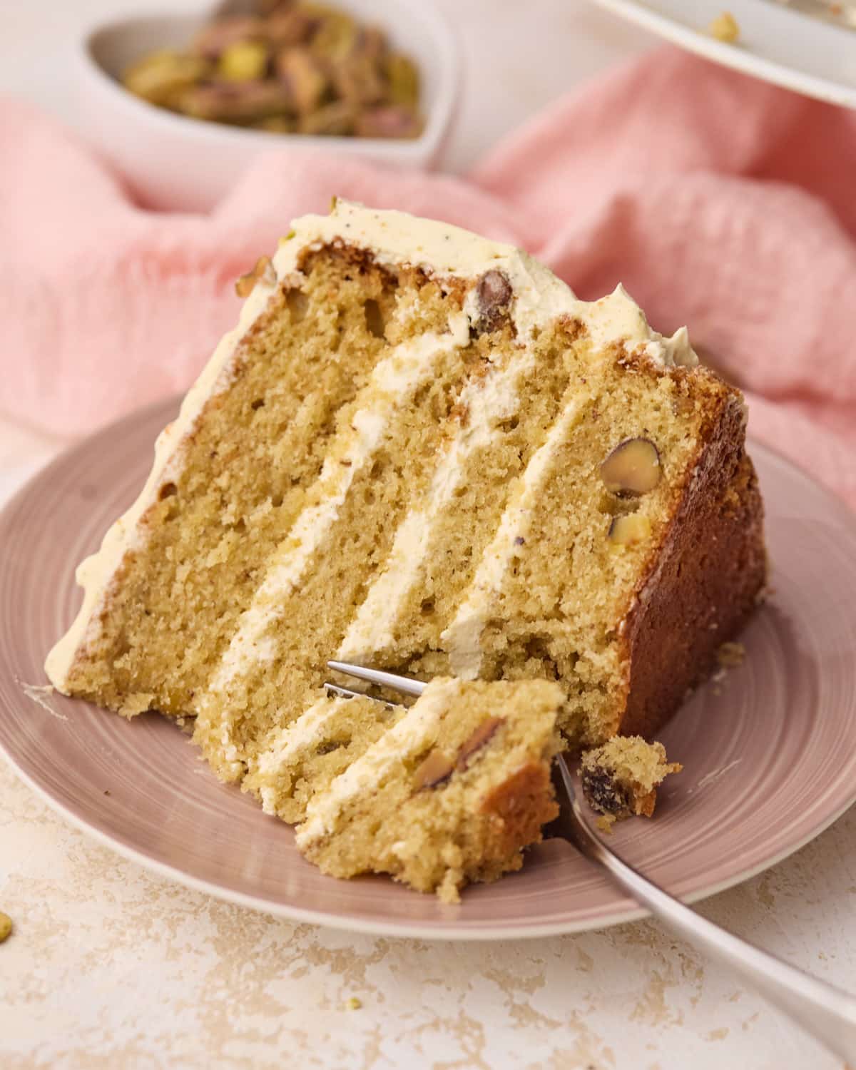 Single slice of pistachio cake on a pink plate with a forkful being taken out of it, showing the silky smooth texture of the pistachio buttercream. 