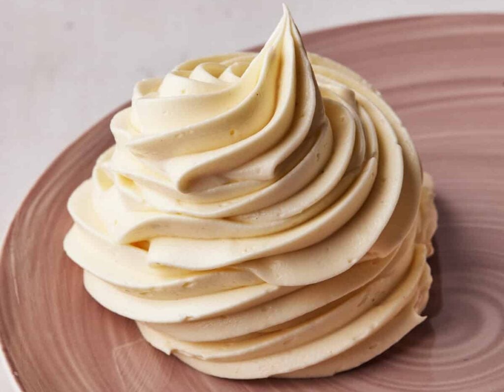 Swirl of russian buttercream piped onto a pink plate to show the silky texture.